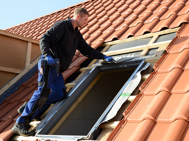 Dachdecker montiert ein modernes Dachfenster auf einem Ziegeldach bei Arbeiten an einem Haus in Flensburg.