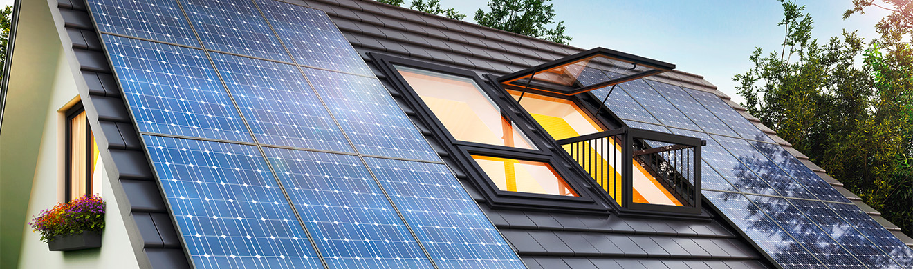 Hausdach mit Solaranlage und modernem Dachfenster unter blauem Himmel in einem Wohngebiet in Flensburg.