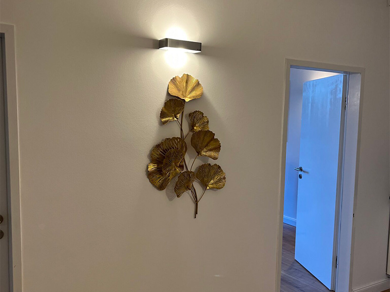 Schlichter Praxisflur mit neutralen Wänden, Wandlampe und dekorativem Element – sauber und professionell.