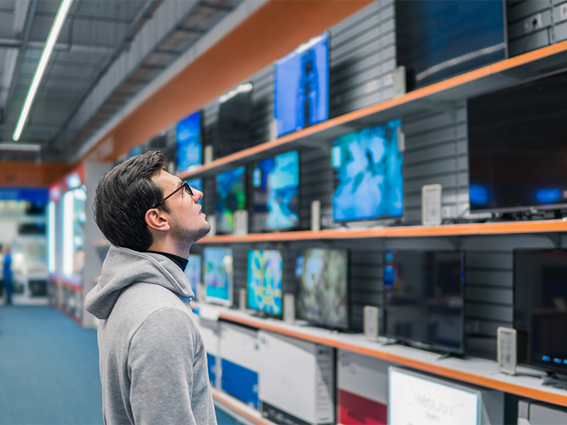Mann betrachtet große moderne Fernseher in einem Elektronikgeschäft und vergleicht aufmerksam verschiedene Bildschirmgrößen und Technologien