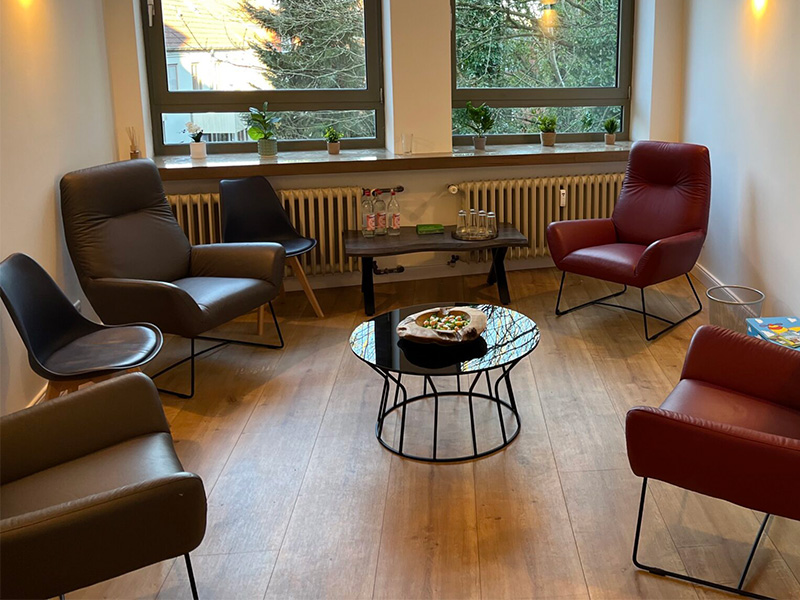 Modernes Wartezimmer mit Sitzbank, Sesseln, Holzboden und großen Fenstern – einladend, freundlich und professionell gestaltet.