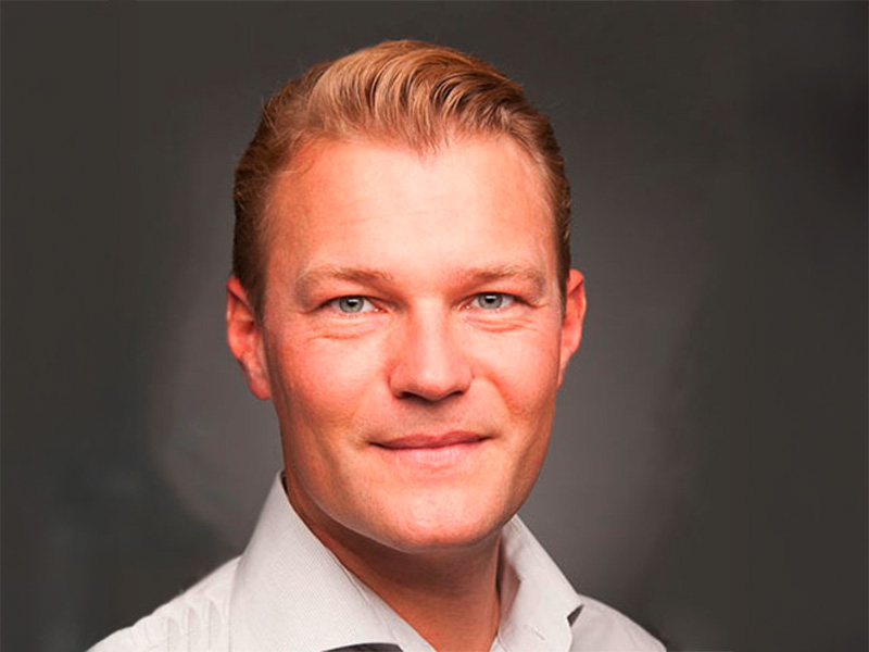 Dr. Guido Wölk blickt freundlich in die Kamera, vor neutralem Hintergrund seiner Praxis in Flensburg.