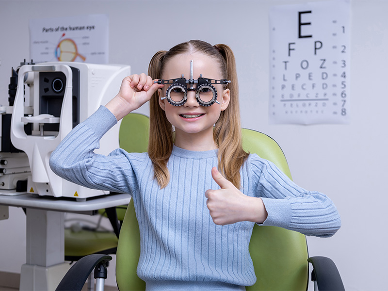 Ein blondes Schulmädchen sitzt bei einem Augenoptiker und schaut bei einem Sehtest in Flensburg durch eine optische Messbrille.