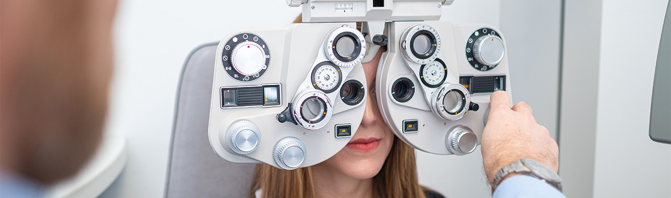 Eine Frau sitzt beim Sehtest im Optikergeschäft und blickt durch ein Phoropter-Gerät zur Augenkontrolle.