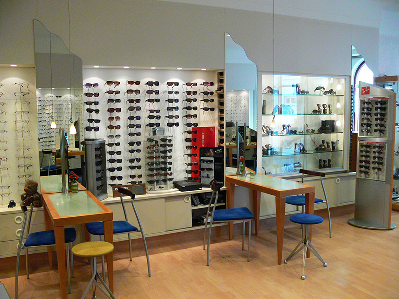 Innenaufnahme bei Optik Gloyer in Flensburg mit Beratungstischen vor einer Wand voller Brillengestelle.
