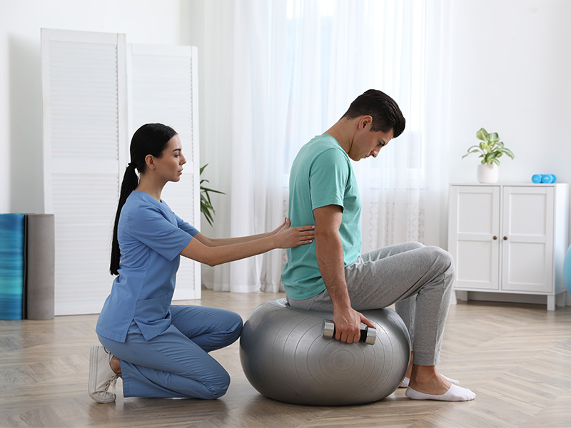 Orthopäde begleitet Patientin bei Übungen mit Hantel zur Krankengymnastik Skoliose in moderner physiotherapeutischer Behandlungssituation.