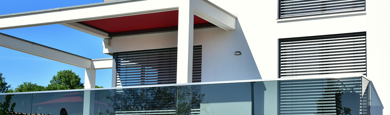 Moderner Balkon mit Pergola und Glasgeländer als stilvoller Sonnenschutz für Außenbereiche an einer Hausfassade